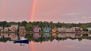 A row of colorful houses along a calm lake with a rainbow reflection.