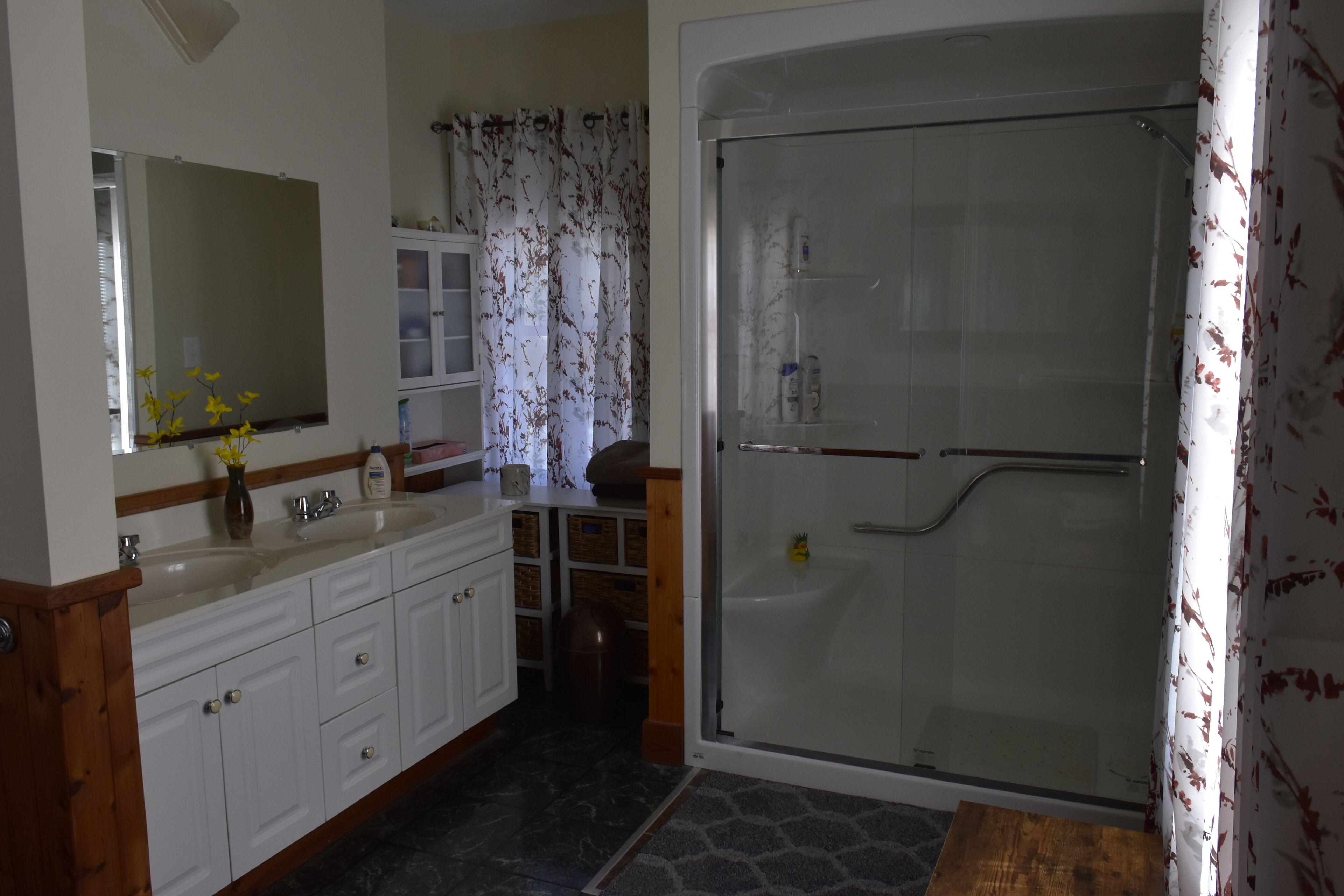 Une salle de bain avec une douche à parois de verre, un lavabo blanc avec un miroir et un meuble-lavabo en bois.