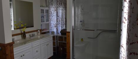 A bathroom with a glass shower enclosure, a white sink with a mirror, and a wooden vanity.