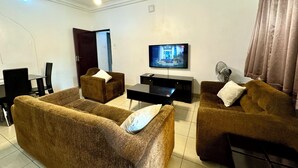 A modern living room with two brown sofas, a black coffee table, and a flat-screen TV mounted on the wall.