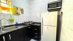 A compact kitchen with a sink, stove, and refrigerator, featuring white tiled walls and black cabinets.