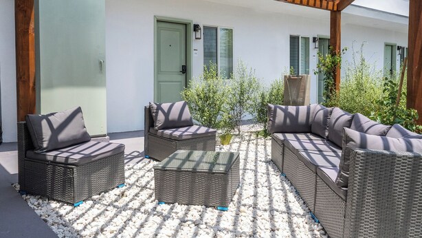 A covered outdoor seating area with wicker furniture and a stone-tiled floor. - The LEEF Hotel (Glendale)