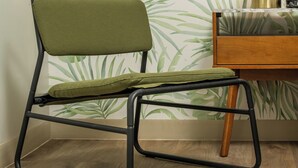 A chair with a metal frame and green upholstery, positioned in front of a wall with a leafy wallpaper pattern. - The LEEF Hotel (Glendale)