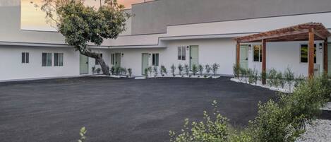 A modern building with a flat roof, a covered outdoor seating area, and a large open driveway.