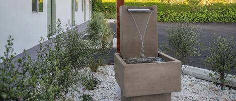 A modern outdoor water feature with a concrete structure, surrounded by white pebbles and small shrubs.