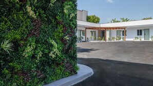 A modern building with a large, lush vertical garden on the left side, a covered outdoor seating area, and a clear sky. - The LEEF Hotel (Glendale)