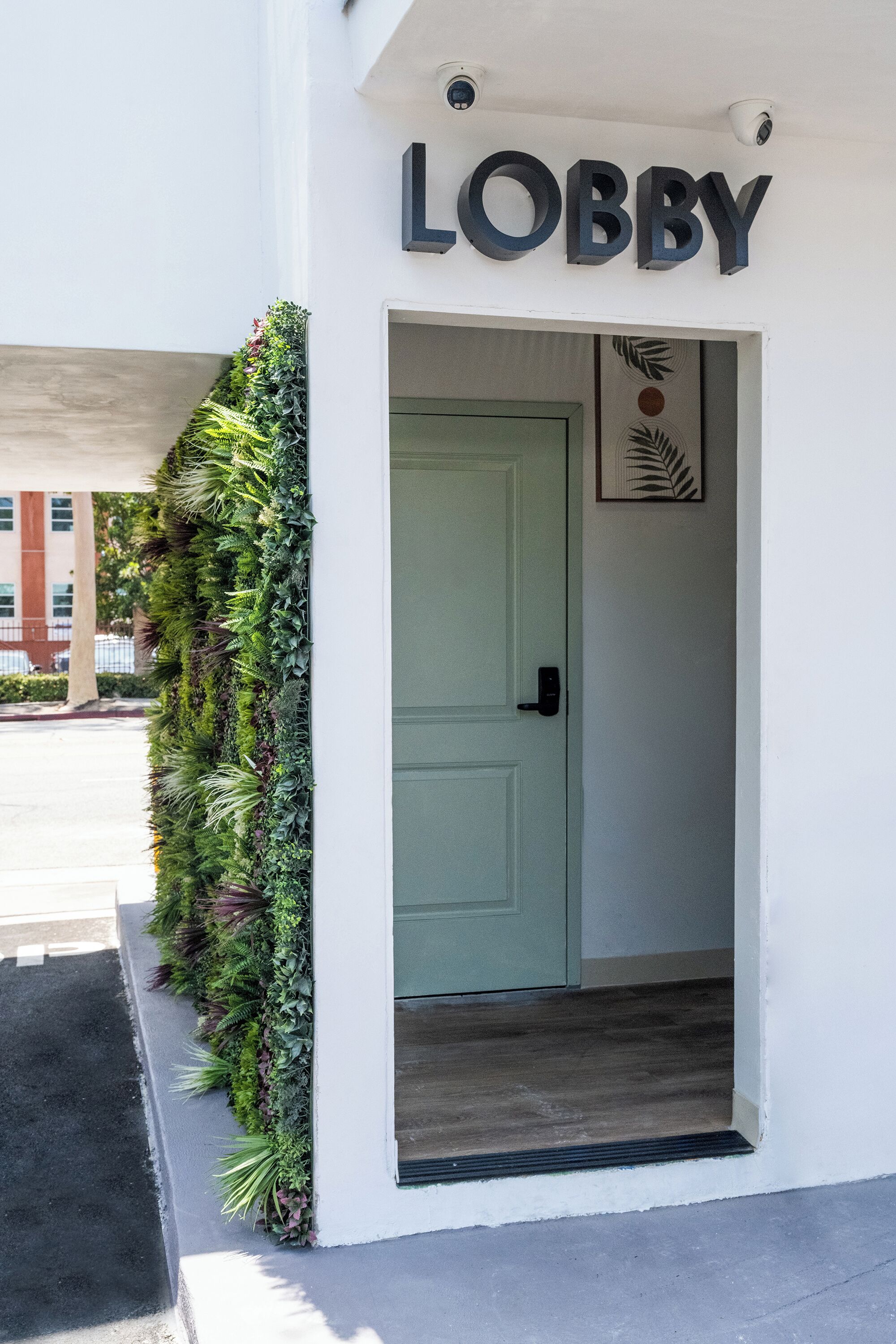 En entréhall med en grön dörr, en skylt ovanför som visar texten ”LOBBY”, och en vertikal trädgård på vänster sida.