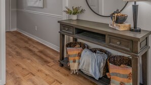 A hallway with a wooden floor, a dark wooden console table with baskets, a mirror, and a hanging light fixture.