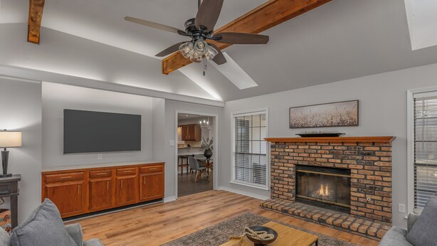 A living room with a fireplace, a ceiling fan, and a television mounted on the wall.