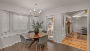 A dining area with a round table, six chairs, a vase with greenery, and a chandelier.