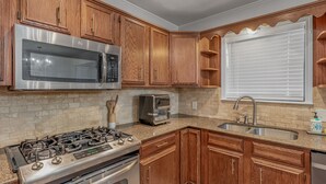 A kitchen with wooden cabinets, a stainless steel microwave, a toaster, a gas stove, and a sink.