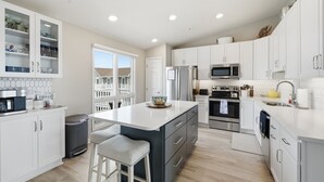 A modern kitchen with white cabinets, stainless steel appliances, and a large island with bar stools. - Bayfront Coastal Paradise | Pool | Beach Access (Bethany Beach)