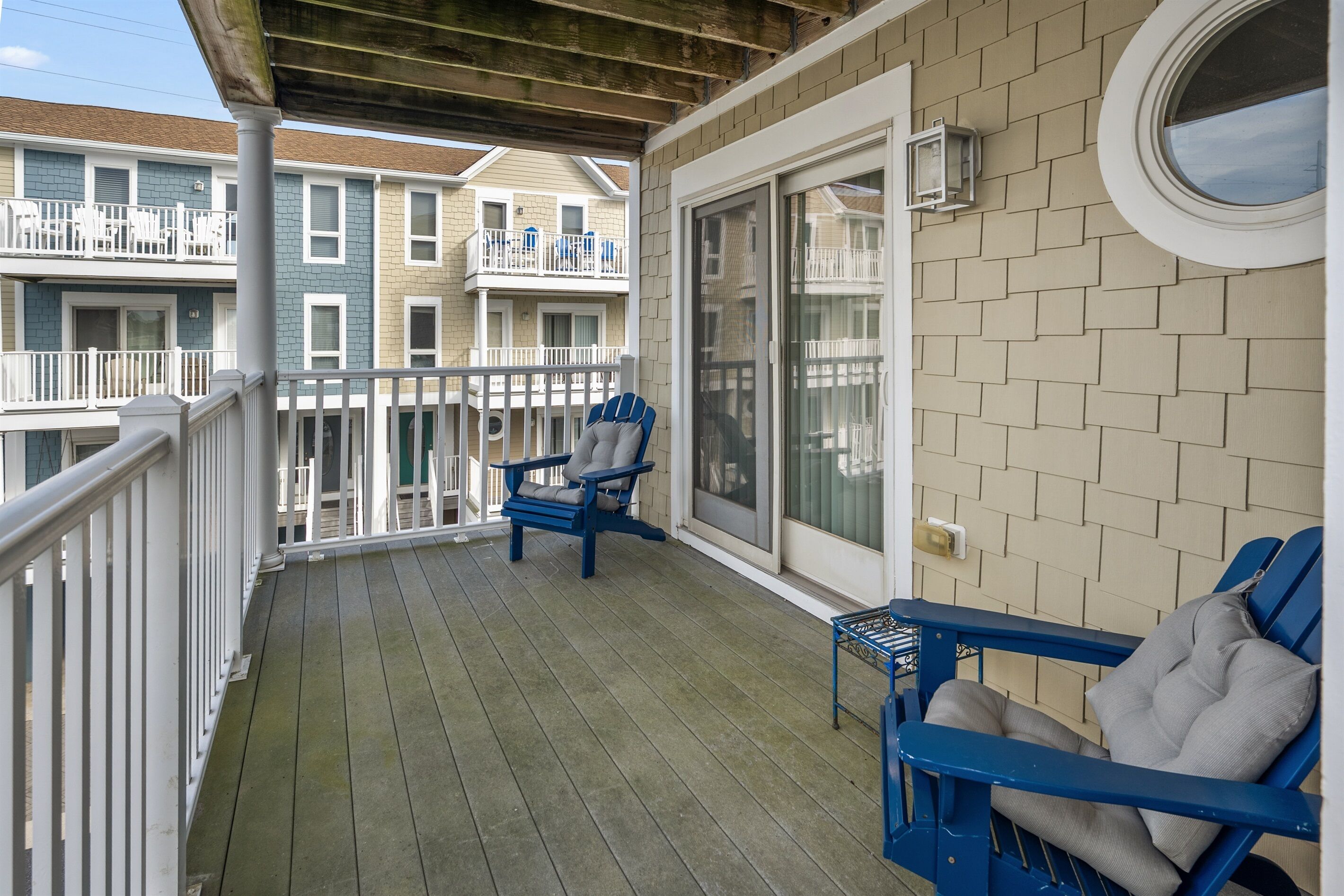 A wooden deck with blue Adirondack chairs and a small table, overlooking a row of townhouses.