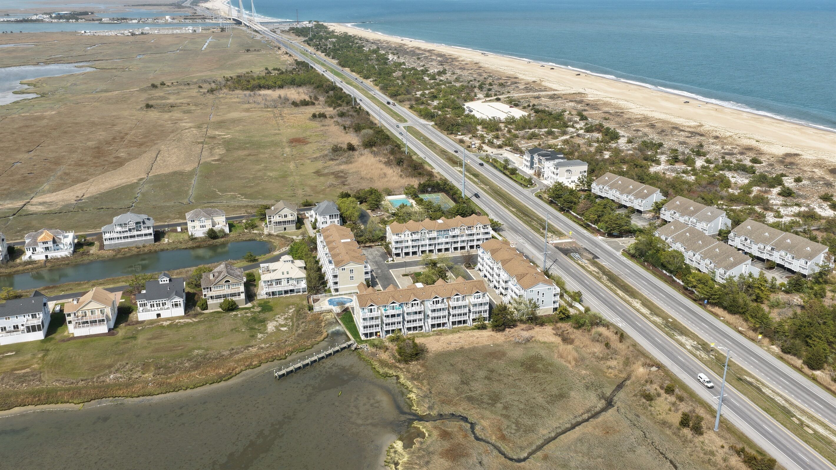An aerial view of a coastal residential area with houses, a beach, and a bridge.