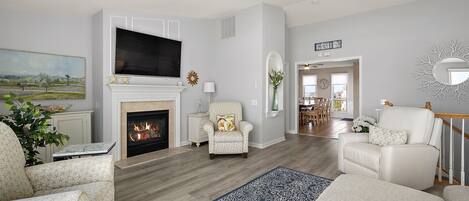 Una sala de estar con chimenea, televisor y una escalera que lleva a otra habitación.