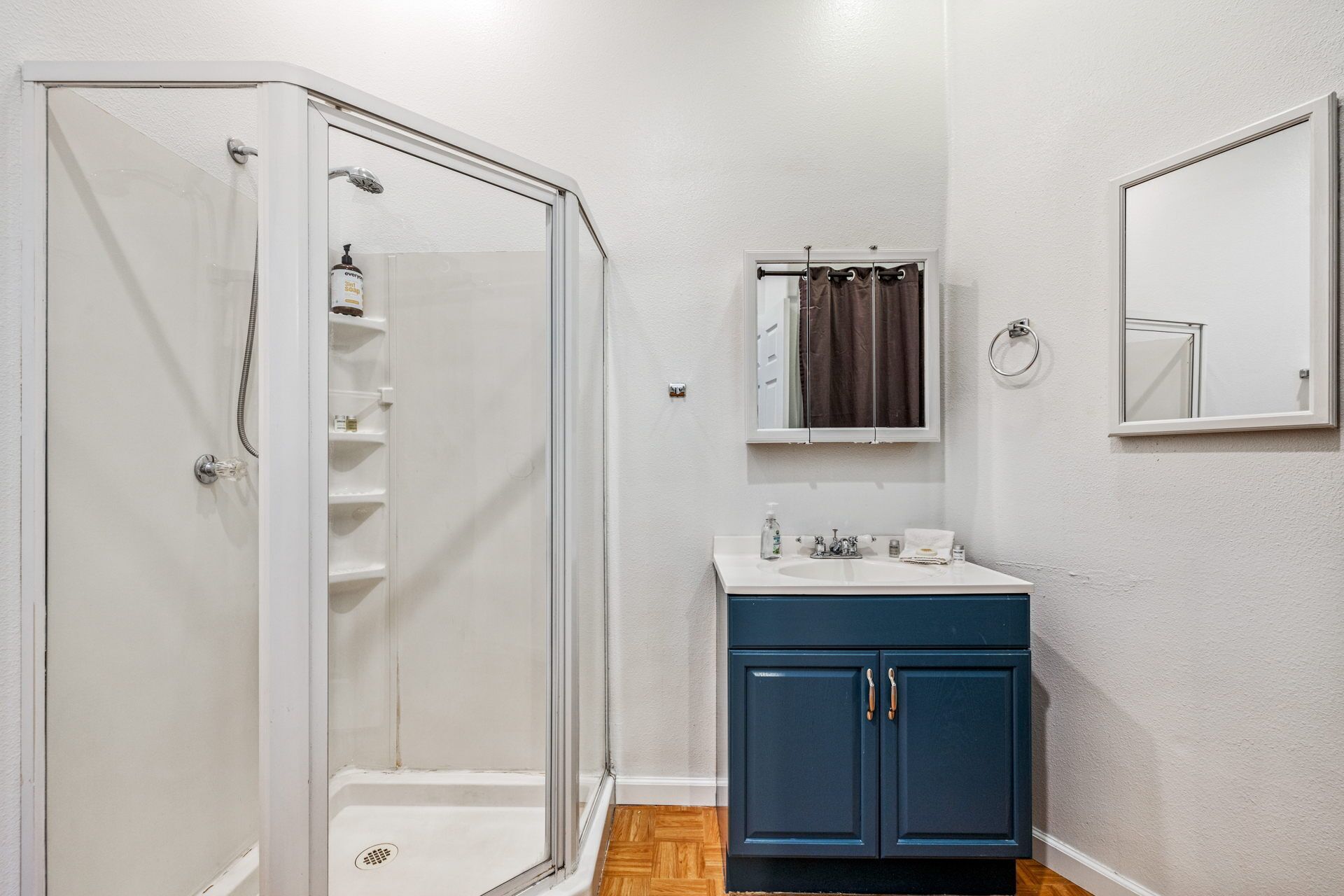 A bathroom with a glass-enclosed shower, a white sink with a blue cabinet, and a mirror above the sink.