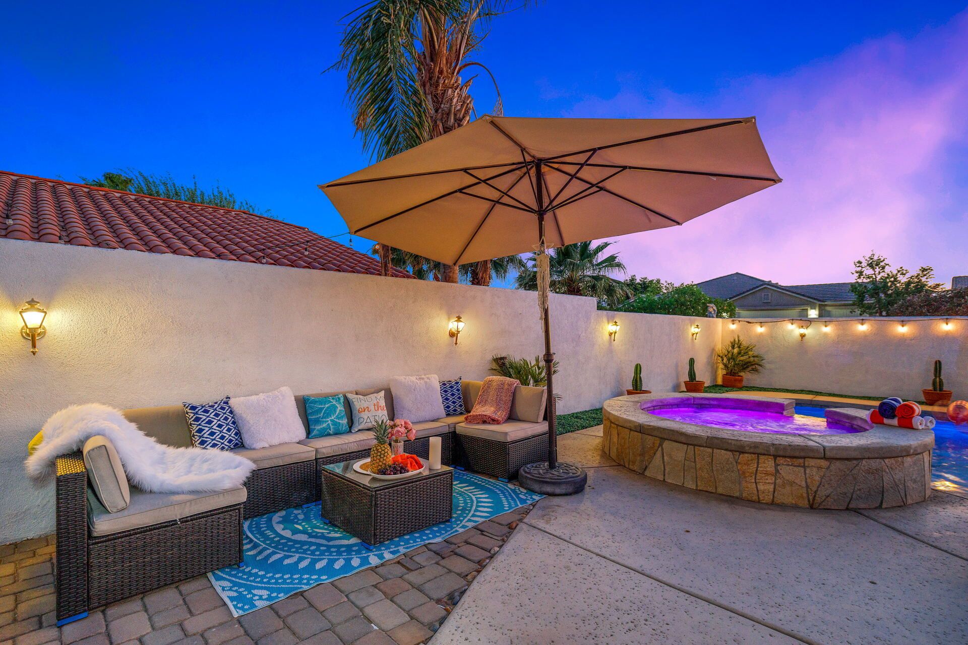 A patio with wicker furniture, a hot tub, and string lights.
