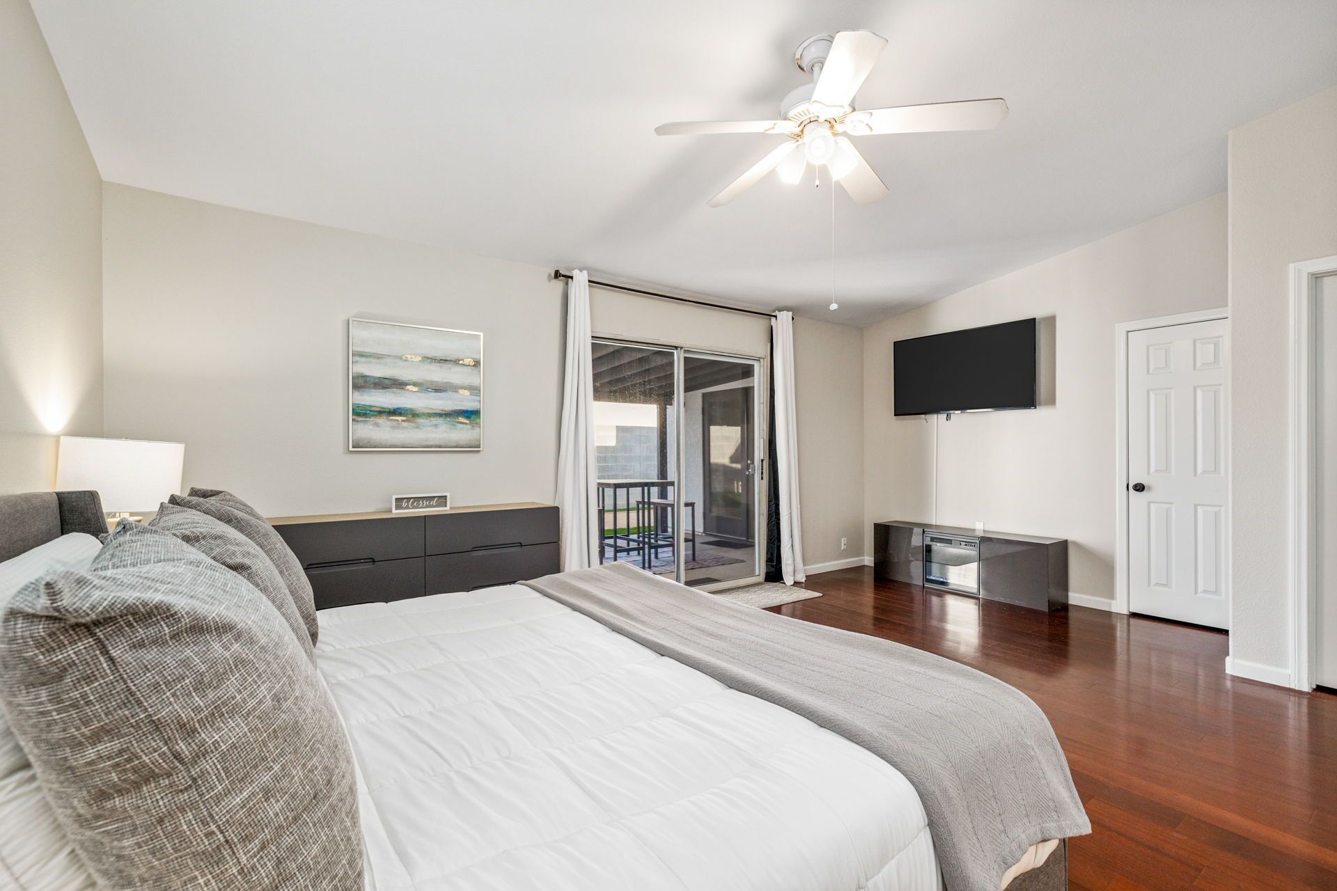 Ein Schlafzimmer mit einem Bett, einem Deckenventilator, einem Fernseher und einer Glasgleittür, die zu einem Balkon führt.