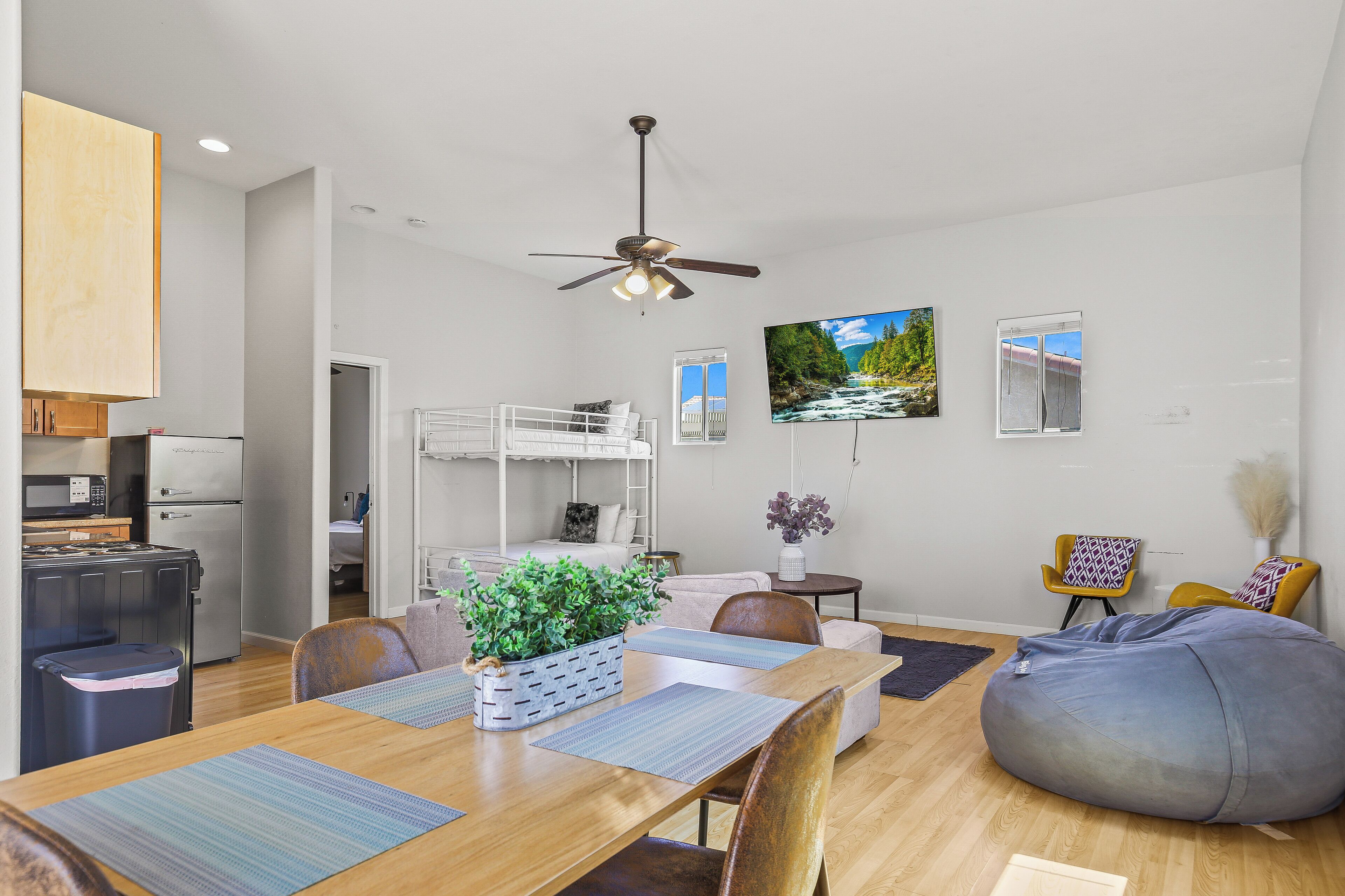 Una sala de estar moderna con comedor, ventilador de techo, televisor y ventana con vista al río.