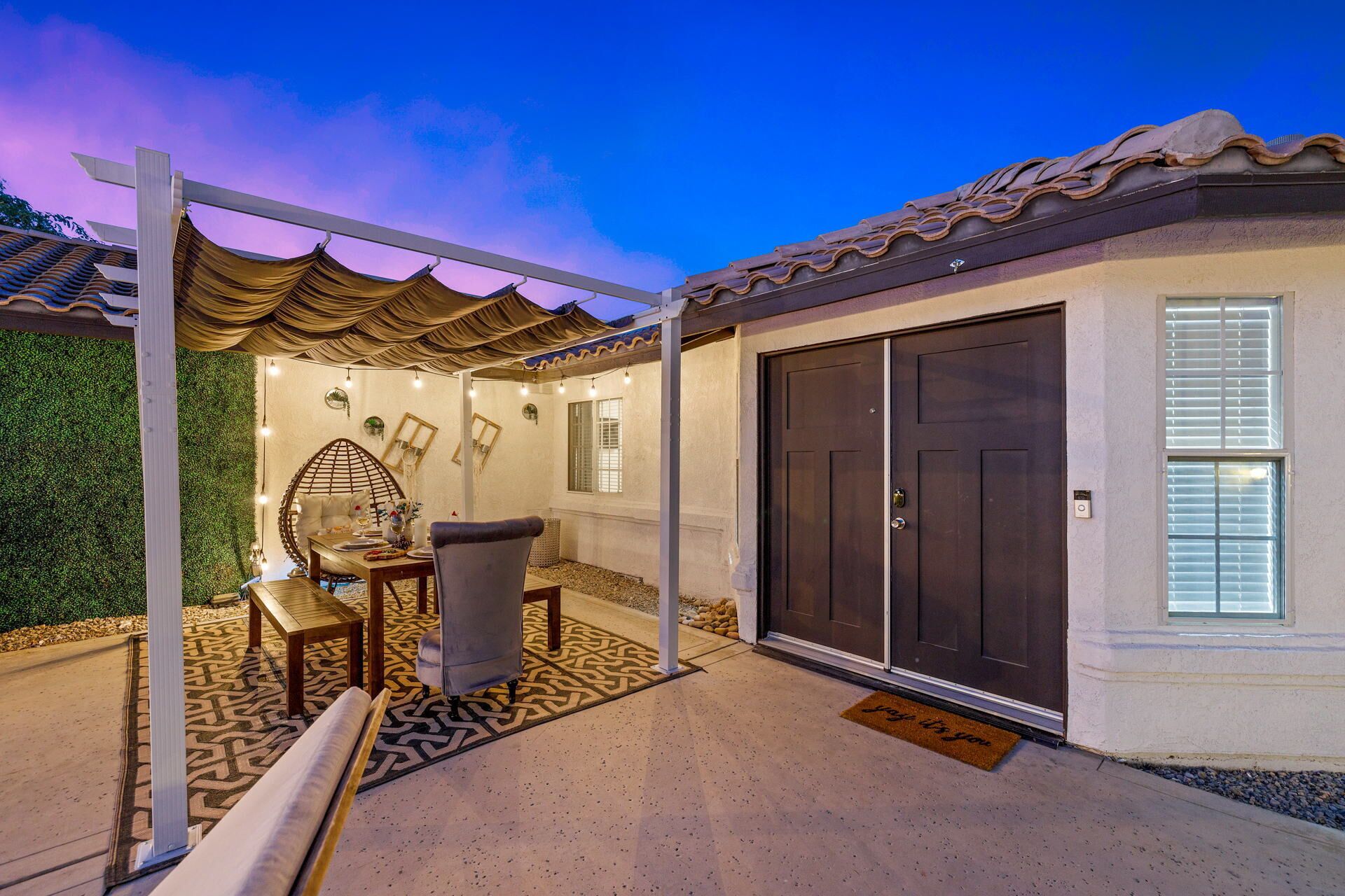 Un espacio de patio cubierto con mesa, sillas y un muro decorativo.