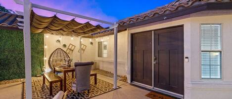 Un espacio de patio cubierto con mesa, sillas y un muro decorativo.
