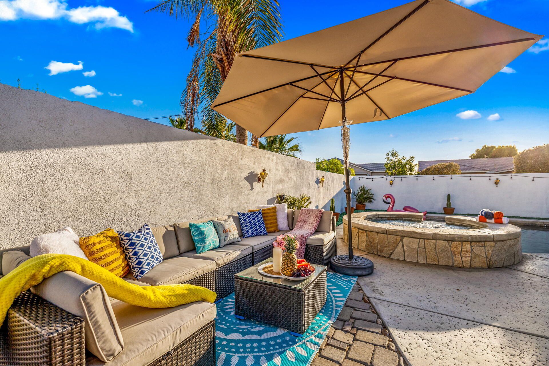 Eine Terrasse mit einer Couch, Kissen, einem Tisch mit Früchten, einem Flamingo-Schwimmding und einem Whirlpool.