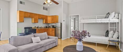 A modern living space with a sofa, a dining table, a kitchen area, and a bunk bed.