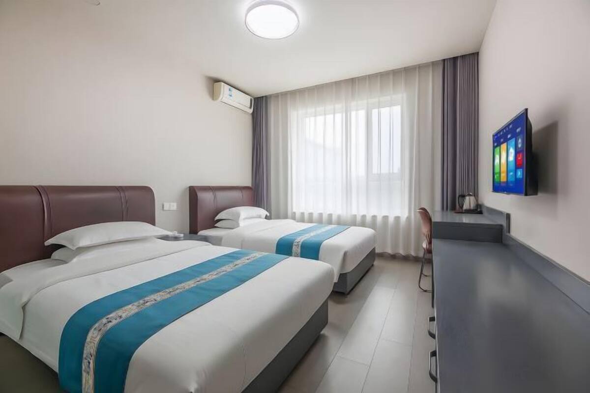 Une chambre d’hôtel avec deux lits, un bureau, une télévision et une fenêtre avec des rideaux.