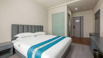 A hotel room with a bed, a nightstand, a desk, and a door.