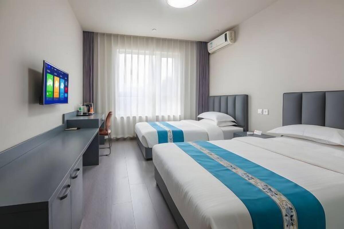 Une chambre d’hôtel avec deux lits, un bureau, une télévision et une fenêtre avec des rideaux.