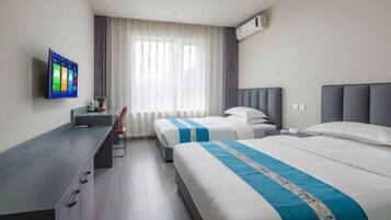 A hotel room with two beds, a desk, a TV, and a window with curtains.