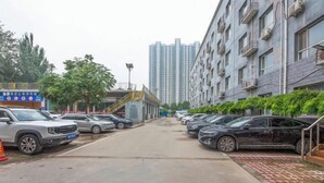 Un parking où de nombreuses voitures sont garées de part et d’autre, un immeuble doté de balcons et, au fond, un gratte-ciel.