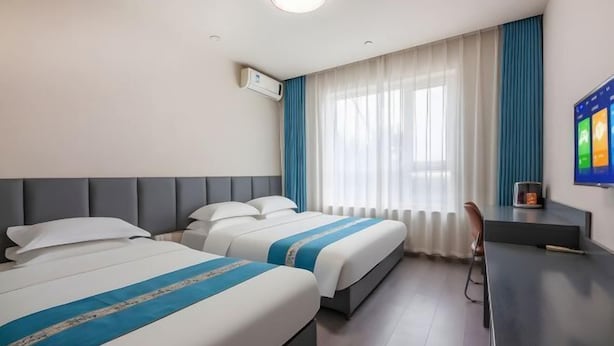 Ein Hotelzimmer mit zwei Betten, einem Schreibtisch, einem Sessel, einem Fernseher und einem Fenster mit Vorhängen.