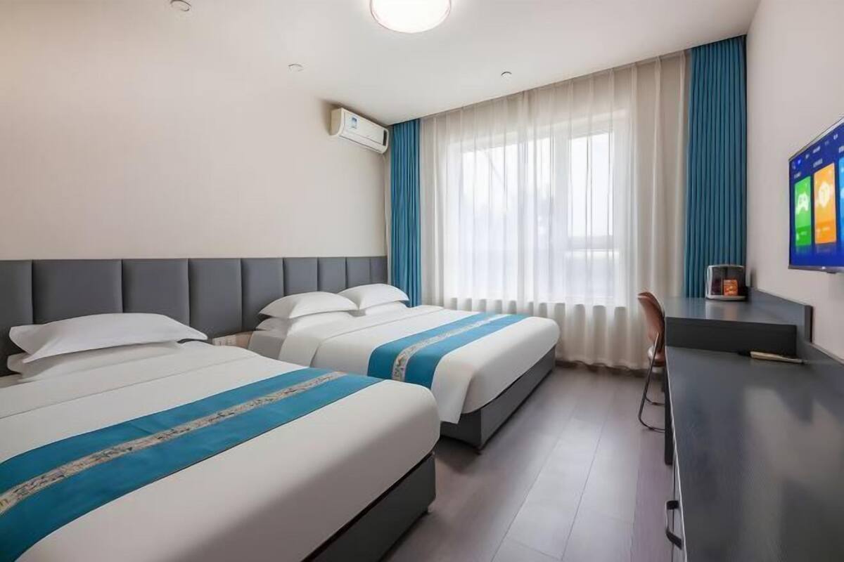 Une chambre d’hôtel avec deux lits, un bureau, une chaise, une télévision et une fenêtre avec des rideaux.