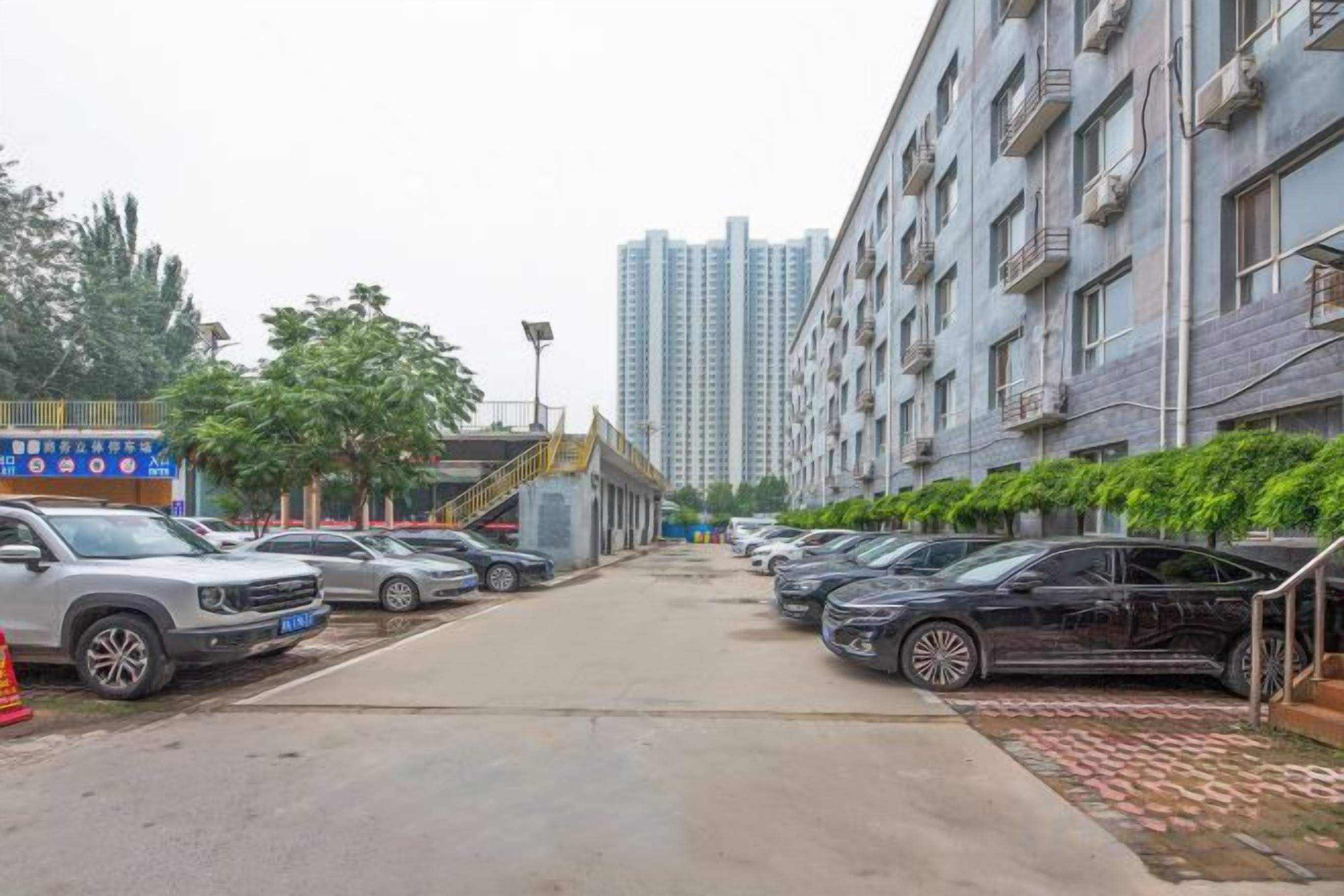 A parking lot with cars, a building with balconies, and a staircase leading to an upper level.