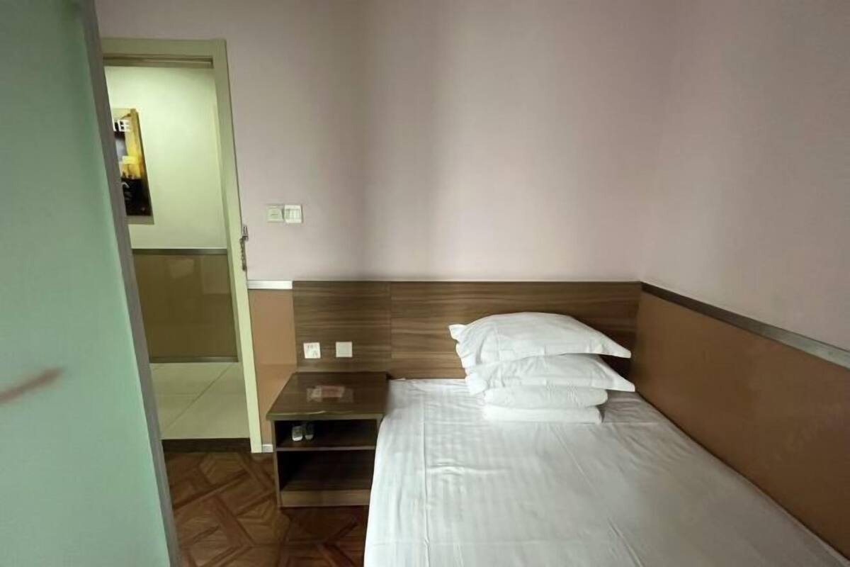 Ein Hotelzimmer mit einem Einzelbett, einem Holznachttisch und einer Tür zu einem anderen Raum.