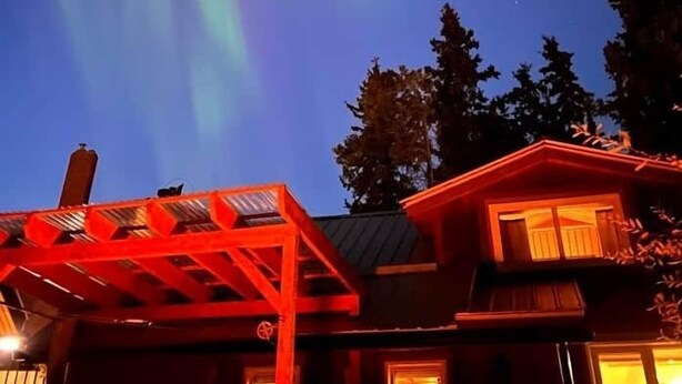 Ett hus med ett rött, upplyst tak och röda fönster, under en natthimmel där gröna norrsken dansar.