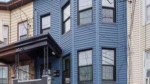 Une maison à deux étages, à l’extérieur bleu foncé, dotée d’un porche à l’avant et de fondations en pierre.