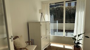A room with a large window, a white wardrobe, a wicker chair, a round rug, and a potted plant. - In the heart of Haltern (Haltern am See)