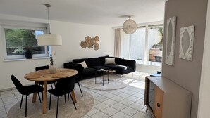 A modern living room with a black sofa, a round wooden dining table with black chairs, a white rug, and a large window with curtains. - In the heart of Haltern (Haltern am See)