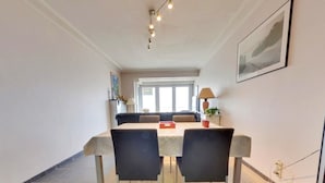 A dining area with a table, chairs, and a rug. There is a window in the background. - Apartment in Middelkerke With Sea View (Middelkerke)