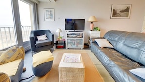 A living room with a sofa, armchair, and a TV stand with a television. - Apartment in Middelkerke With Sea View (Middelkerke)