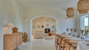 A spacious dining area with a long table set for a meal, a fireplace in the background, and a wooden cabinet with a lamp on the left. - Casa Iris (Javea / Xàbia)