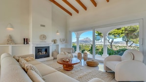 A modern living room with a large sofa, a round coffee table, and a fireplace. There are large windows offering a view of the outdoors. - Casa Iris (Javea / Xàbia)