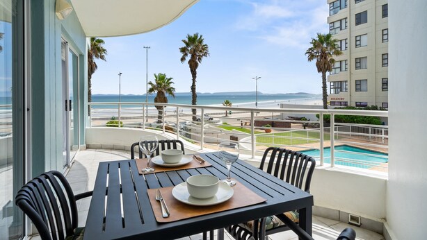 Ein Balkon mit Tisch für zwei Personen, mit Blick auf Pool und Strand.