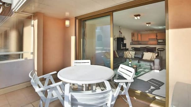 A balcony with a round table and white chairs, a sliding glass door leading to a living area with a sofa and a coffee table. - Charming 2 bedroom Apt/Balcony/Parking/by Marina+Shops (Antibes)