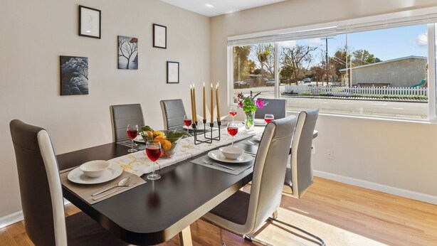 Un comedor con una mesa dispuesta para cuatro personas, con un diseño moderno que incluye una mesa negra, sillas blancas y vistas al exterior a través de amplios ventanales.