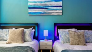 Un dormitorio con dos camas, una mesita de noche con lámpara y un cuadro abstracto azul en la pared.