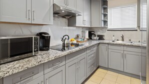 Una cocina moderna con gabinetes grises, una campana extractora de acero inoxidable, un microondas integrado y un lavamanos.
