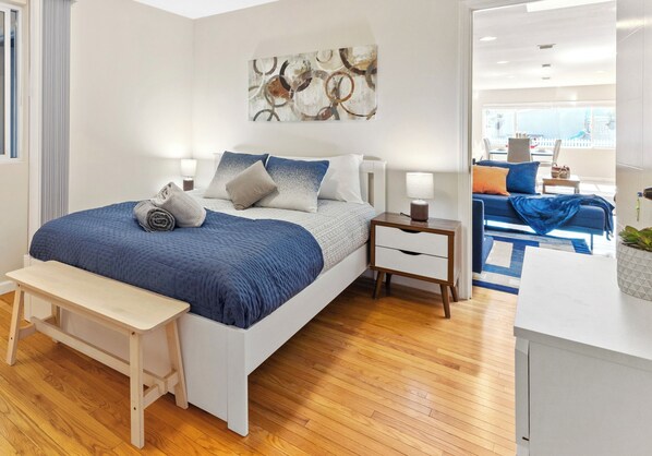 A modern bedroom with a bed, bedside tables, a bench, and a view of the living area.